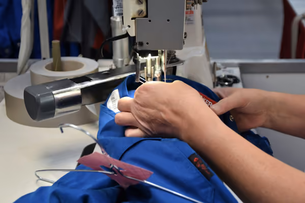 Hands guiding fabric through an industrial sewing machine during alterations
